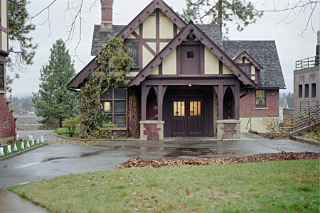 [A small two-story building similar in styling to the house with gabled roofs and dark wood on light background on upper floors with the first floor being brick.]